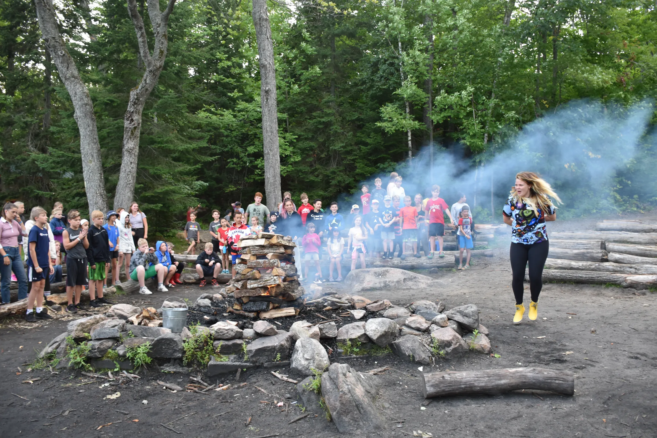 Smoke billows from a campfire as a counsellor leads the group in a song