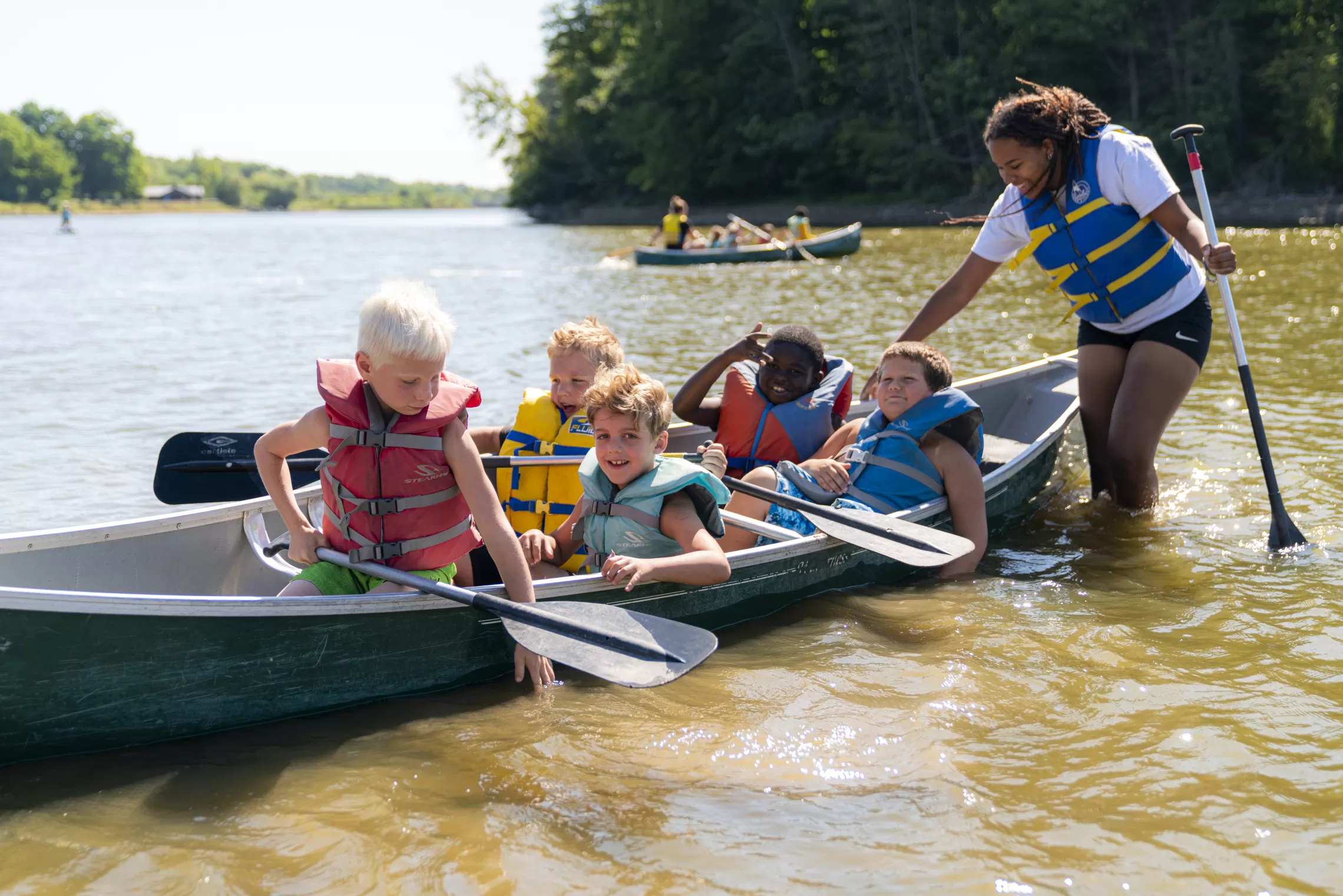 a group of smiling campers is sitting in a canoe on Christie Lake in the summer time.