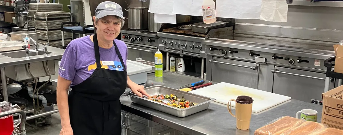 elderly woman with short grey hair in a commercial kitchen preparing vegetables