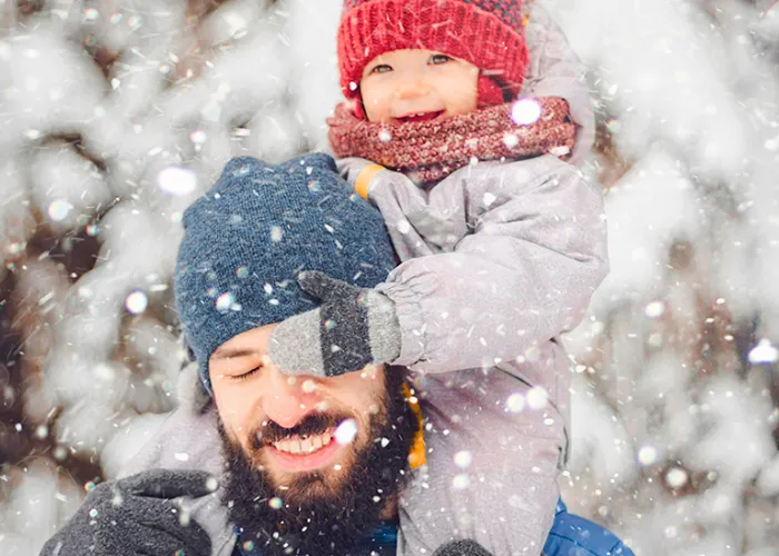 Father holding child on shoulders while snowing