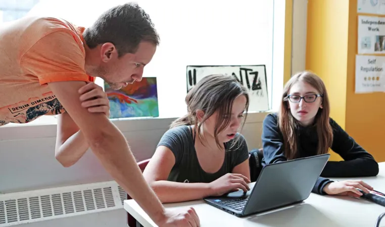 two students working on a laptop with an instructor