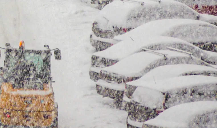 snow falling on cars with snowplow going past