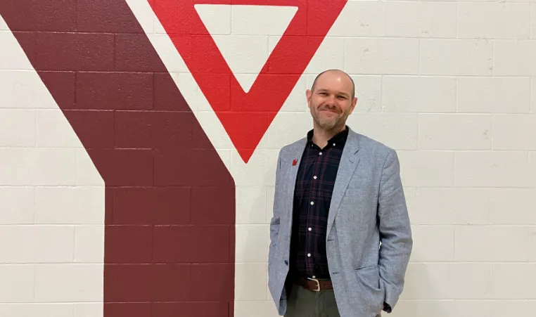 Man in sports jackets stands in front of YMCA logo