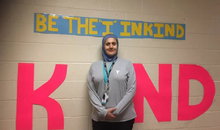 YMCA child care supversior in front of a sign that says "Be the I in Kind"