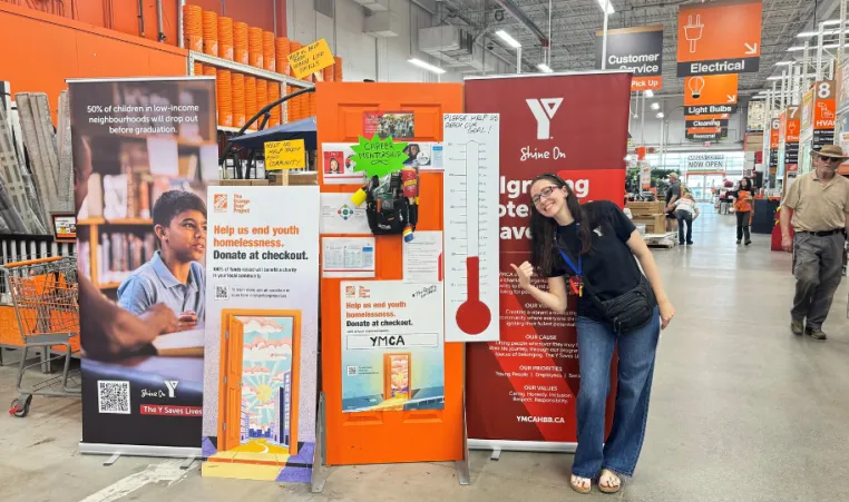 a ymca employee gives a thumbs up infront of a fundraising thermometer