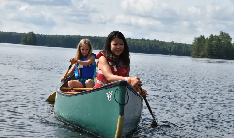 two girls paddle in a canoe on a lake