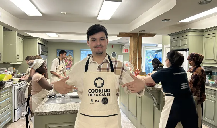 Elham pointing to his Cooking for a Cause apron in the Mark Preece House kitchen