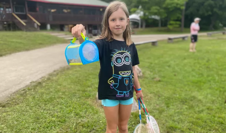 girl holding a bucket of bugs at a summer camp
