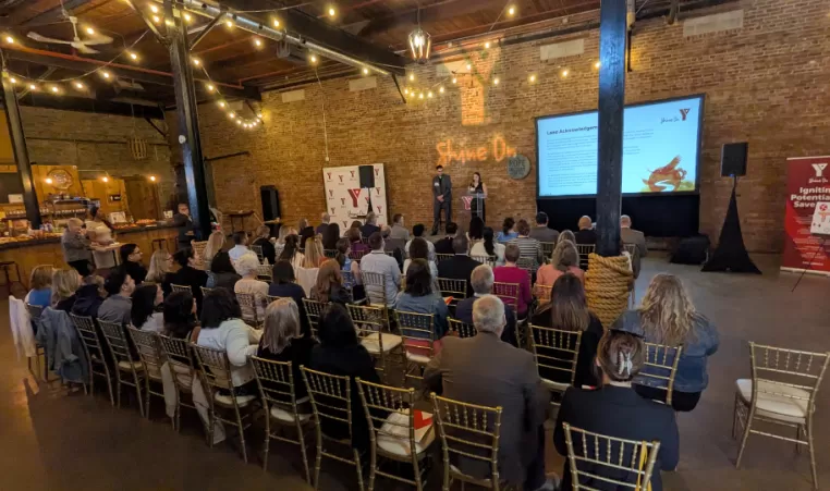 dozens of people sit and watch a presentation by the YMCA