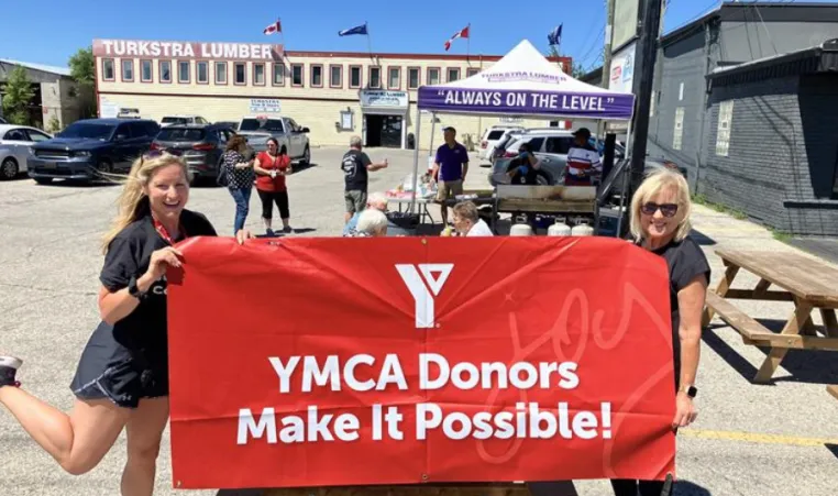 YMCA staff hold up donor banner in front of charity BBQ