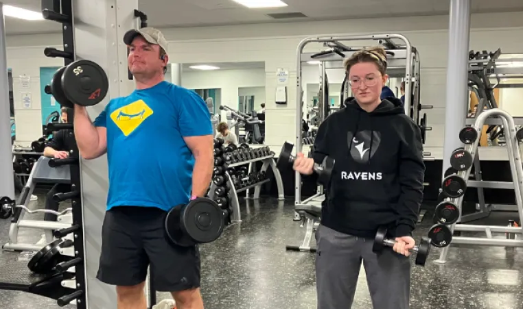 Father and daughter lift weights together in fitness centre