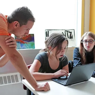 two students working on a laptop with an instructor