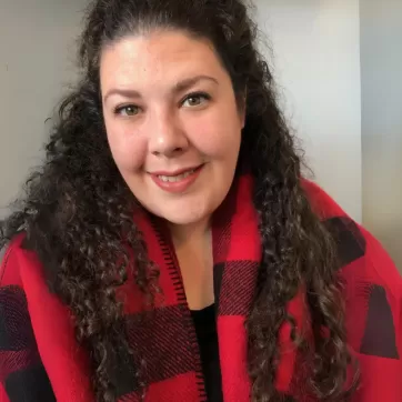 Jacqueline is wearing a red and black sweater and smiling at the camera.
