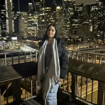 Young woman poses against the backdrop of a downtown city with skyscrapers at night.