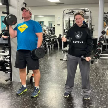 Father and daughter lift weights together in fitness centre