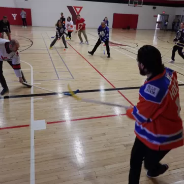 adults in gym playing floor hockey