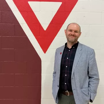 Man in sports jackets stands in front of YMCA logo