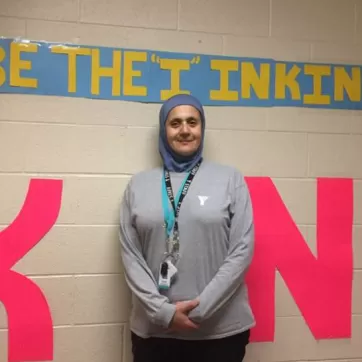 YMCA child care supversior in front of a sign that says "Be the I in Kind"