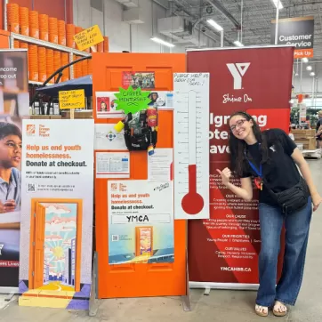 a ymca employee gives a thumbs up infront of a fundraising thermometer