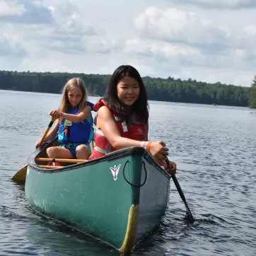 two girls paddle in a canoe on a lake