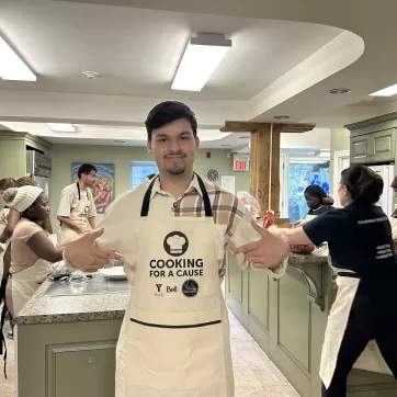 Elham pointing to his Cooking for a Cause apron in the Mark Preece House kitchen