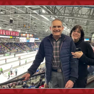 Women stands behind man as they smile at camera in front of the Brier curling championship
