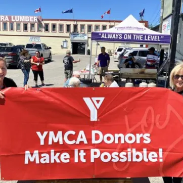 YMCA staff hold up donor banner in front of charity BBQ
