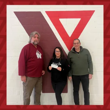 two men and one woman pose in front of YMCA logo