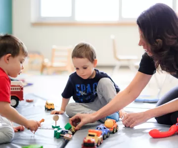 Two male preschool children and Educator playing with toy cars
