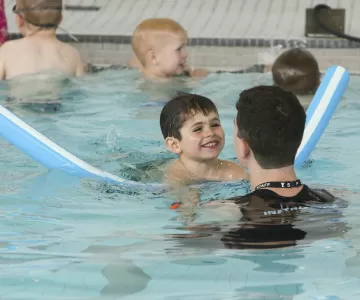 Child swimming with pool noodle and instructor
