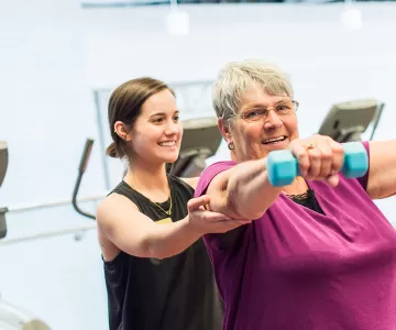 Senior female member light weight training with YMCA fitness coach