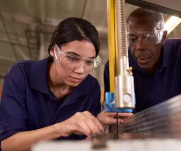 young person learning how to use jigsaw, being taught by older carpenter.