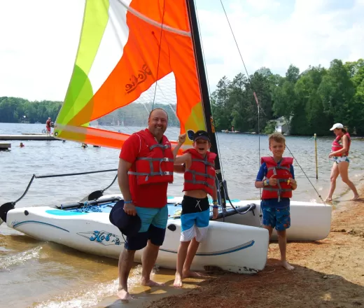 Father and sons standing in front of hobie cat on water