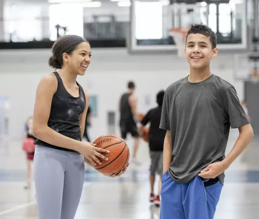 two young people holding basketball in gym laughing