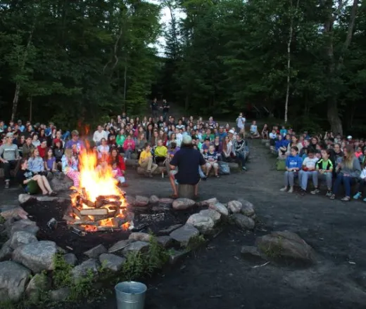 A campfire burns bright while a counsellor tells a story to Wanakita campers