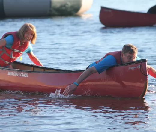 An adult male and female paddle a canoe using their hands