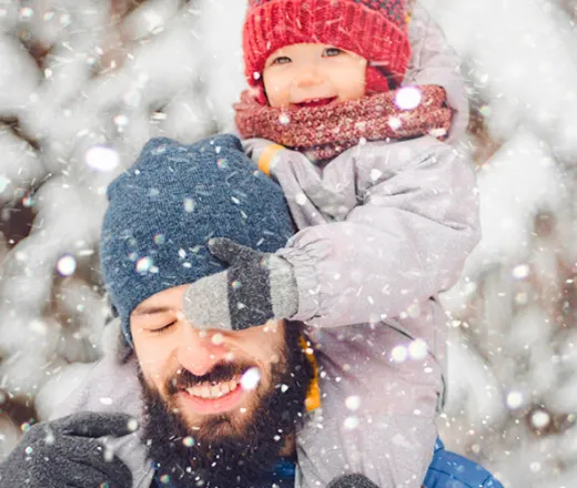 Father holding child on shoulders while snowing
