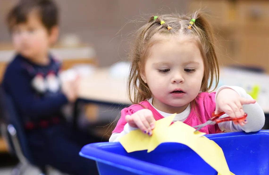 Female preschool child making crafts using paper and scissors