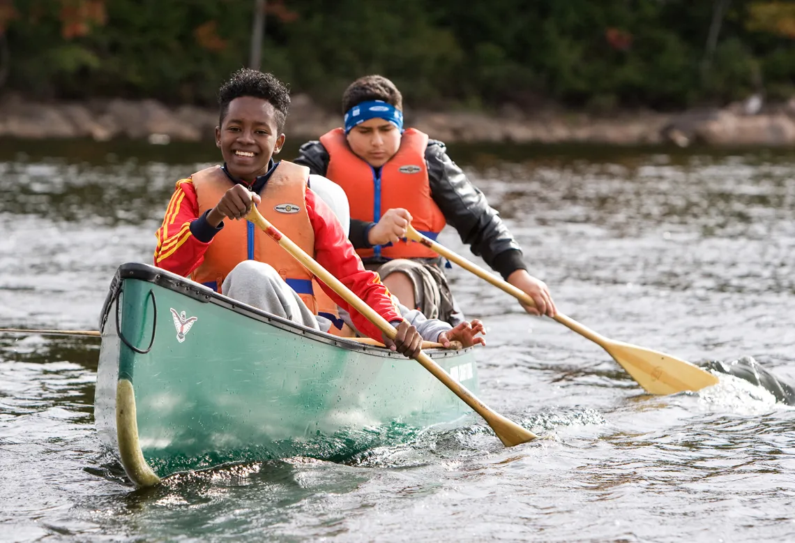 Two smiling youths paddling a canoe during Fall programming at Wanakita