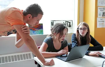 two students working on a laptop with an instructor