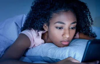 young girl looking at phone in dark room, frowning
