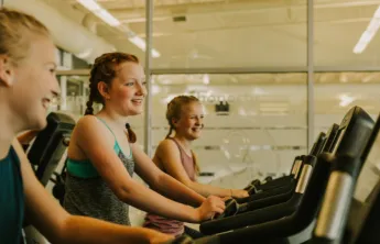 three girls on treadmills smiling