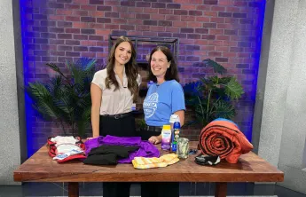 Two women smiling behind a table of camping supplies