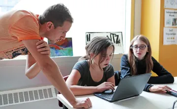 two students working on a laptop with an instructor
