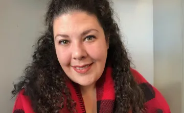 Jacqueline is wearing a red and black sweater and smiling at the camera.