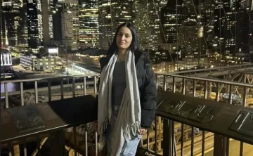 Young woman poses against the backdrop of a downtown city with skyscrapers at night.