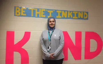 YMCA child care supversior in front of a sign that says "Be the I in Kind"