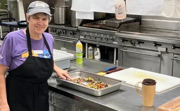 elderly woman with short grey hair in a commercial kitchen preparing vegetables