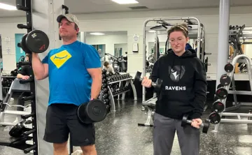 Father and daughter lift weights together in fitness centre