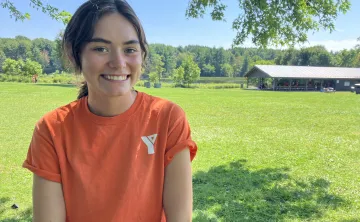 ymca day camp counsellor in orange shirt in font of green space and pavilion